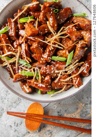 Ginger beef with crispy beef, a lightly sweet sauce, green onion and caramelized ginger closeup in the bowl. Vertical top view Ginger beef with crispy beef, a lightly sweet sauce, green onion and caramelized ginger closeup in the bowl. Vertical top view 127648606