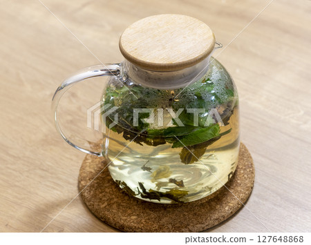 Stylish transparent tea pot with just brewed green tea leaves, mint leaves and lemon slices in it 127648868