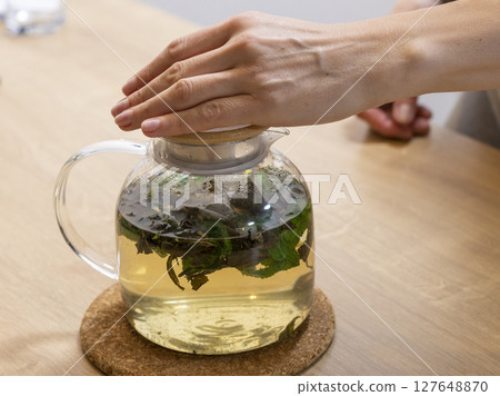 Stylish transparent tea pot with just brewed green tea leaves, mint leaves and lemon slices in it 127648870