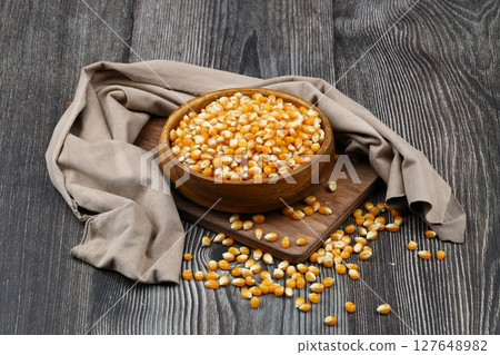 Unpopped popcorn in a wooden bowl on wooden background. A type of corn that expands from the kernel and puffs up when heated. Yellow seeds, edible, raw and vegan food. Isolated macro photo close up. 127648982