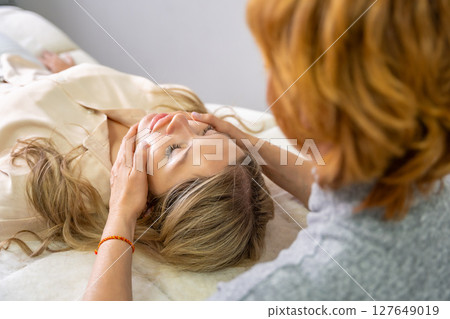 Hands of a female practitioner positioned on the face of a young woman during an Access Bars facial lifting session. Concept of energy work, healing touch and alternative face therapy Hands of a female practitioner positioned on the face of a young woman during an Access Bars facial lifting session. Concept of energy work, healing touch and alternative face therapy 127649019