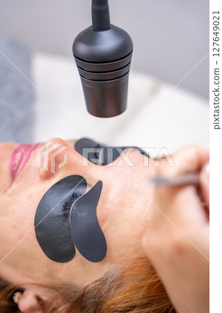 Beautician applying black eye patches before eyelash extension procedure with ultraviolet lamp. Innovative lash extension method in modern beauty salon Beautician applying black eye patches before eyelash extension procedure with ultraviolet lamp. Innovative lash extension method in modern beauty salon 127649021