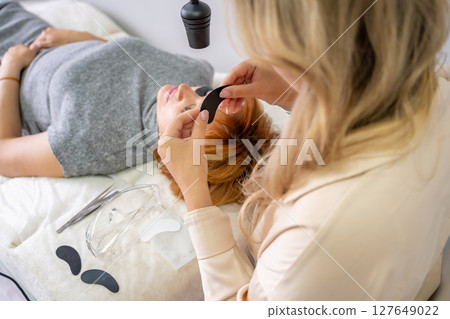 Close-up of beautician hands holding black under-eye patch before UV eyelash extension. Professional tools preparation for modern lash enhancement technique. Close-up of beautician hands holding black under-eye patch before UV eyelash extension. Professional tools preparation for modern lash enhancement technique. 127649022