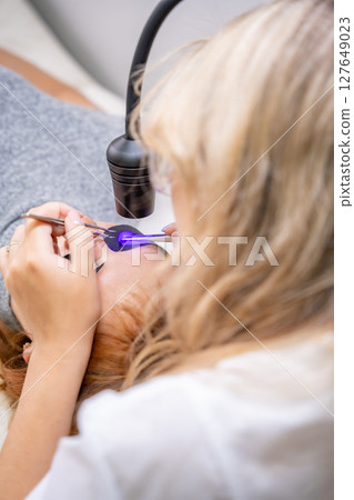 Close up view of eyelash extension procedure using ultraviolet lamp in modern beauty salon. Innovative lash enhancement technology with precise application technique. 127649023