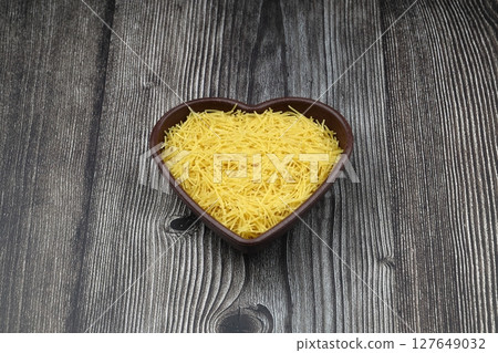 White gluten free vermicelli made from rice flour. Italian pasta in wooden spoon on dark textured background. Top view, space for text. 127649032