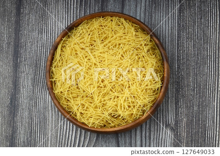 White gluten free vermicelli made from rice flour. Italian pasta in wooden spoon on dark textured background. Top view, space for text. 127649033
