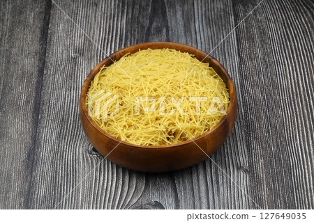 White gluten free vermicelli made from rice flour. Italian pasta in wooden spoon on dark textured background. Top view, space for text. 127649035