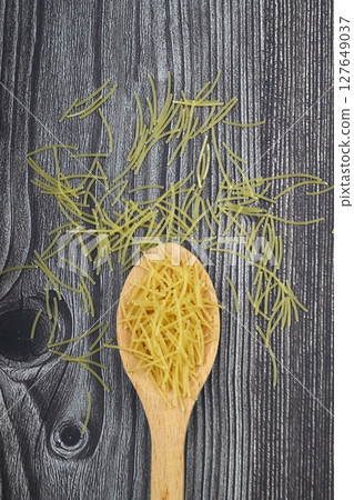 White gluten free vermicelli made from rice flour. Italian pasta in wooden spoon on dark textured background. Top view, space for text. 127649037