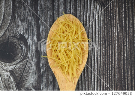 White gluten free vermicelli made from rice flour. Italian pasta in wooden spoon on dark textured background. Top view, space for text. 127649038