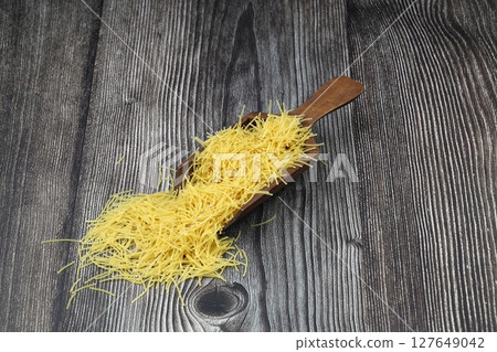 White gluten free vermicelli made from rice flour. Italian pasta in wooden spoon on dark textured background. Top view, space for text. 127649042