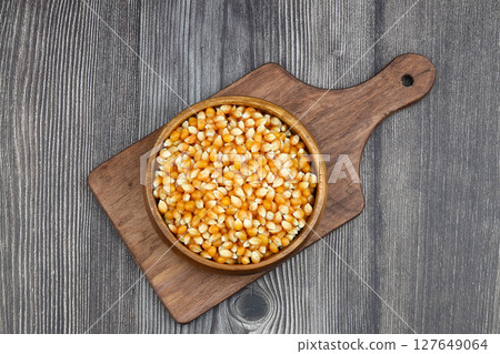 Unpopped popcorn in a wooden bowl on wooden background. A type of corn that expands from the kernel and puffs up when heated. Yellow seeds, edible, raw and vegan food. Isolated macro photo close up. 127649064