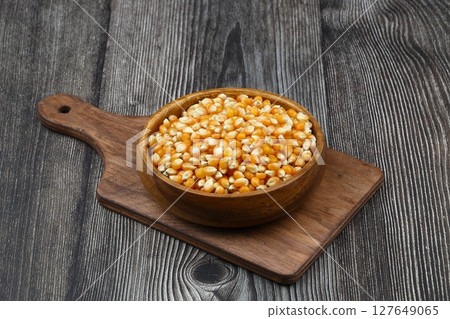 Unpopped popcorn in a wooden bowl on wooden background. A type of corn that expands from the kernel and puffs up when heated. Yellow seeds, edible, raw and vegan food. Isolated macro photo close up. Unpopped popcorn in a wooden bowl on wooden background. A type of corn that expands from the kernel and puffs up when heated. Yellow seeds, edible, raw and vegan food. Isolated macro photo close up. 127649065