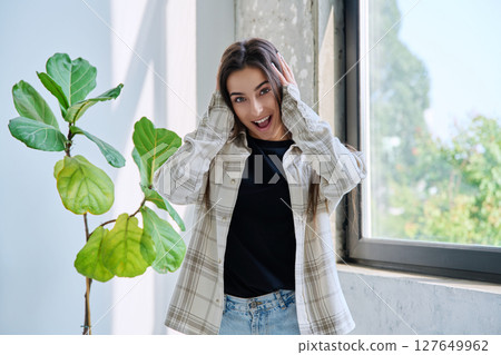 Portrait of beautiful happy teenage girl with open mouth at home near window 127649962