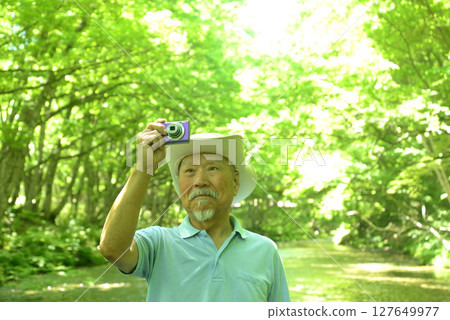 An old man taking pictures of fresh greenery by a clear stream with a digital camera 127649977