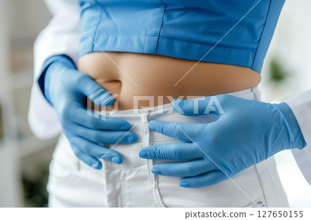 Doctor in blue gloves gently palpates a patient's abdomen, conducting an important health assessment in a clean clinical environment Generative AI 127650155