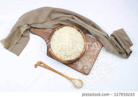 Raw white rice on wooden background. Long uncooked rice in wooden plate. Natural organic food. Traditional Asian cereal culture. 127650283
