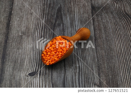Red lentils in wooden scoop, isolated on wooden background. 127651521