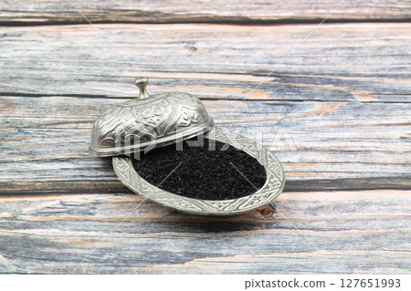 Black cumin seeds and essential oil with bowl and wooden shovel or spoon. Nigella Sativa in glass bottle. Organic herbal medicine for many diseases 127651993
