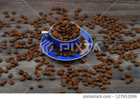 Close-up and top view of hot black coffee in blue coffee cup and roasted Thai coffee beans on wooden background. Close-up and top view of hot black coffee in blue coffee cup and roasted Thai coffee beans on wooden background. 127652099