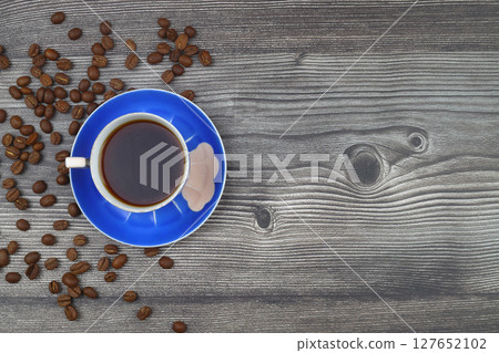Close-up and top view of hot black coffee in blue coffee cup and roasted Thai coffee beans on wooden background. 127652102