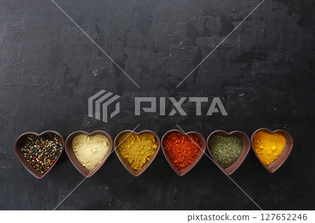 Different kind of spices on a black stone. Oriental spices in in heart shaped bowl, 127652246