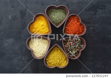 Different kind of spices on a black stone. Oriental spices in in heart shaped bowl, 127652247