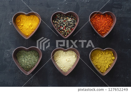 Different kind of spices on a black stone. Oriental spices in in heart shaped bowl, 127652249