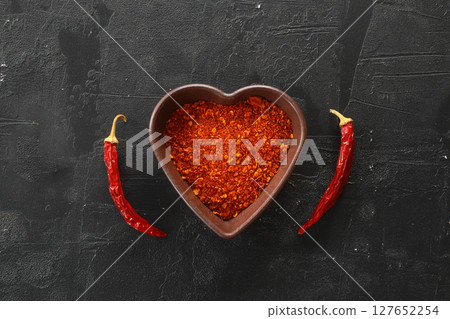red hot chili peppers powder in heart shaped bowl on black stone table. Love concept. Top view red hot chili peppers powder in heart shaped bowl on black stone table. Love concept. Top view 127652254