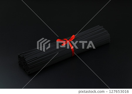 Raw black homemade spaghetti bunch isolated. Dry black noodles macaroni bundle. Close-up Raw black homemade spaghetti bunch isolated. Dry black noodles macaroni bundle. Close-up 127653016