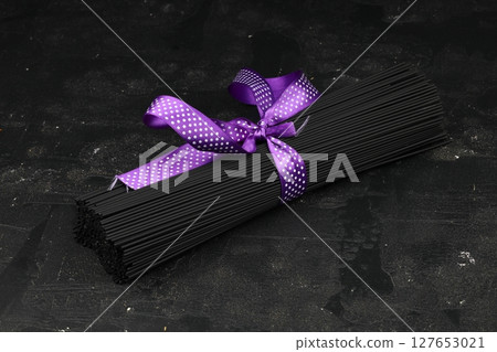 Raw black homemade spaghetti bunch isolated. Dry black noodles macaroni bundle. Close-up 127653021
