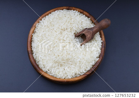 Raw white rice on black background. Long uncooked rice in wooden plate. Natural organic food. Traditional Asian cereal culture. 127653232