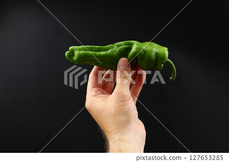 A hand holds a green pepper on a black background. green pepper isolated 127653285