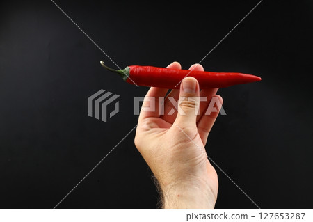 A hand holds a red hot pepper on a black background. Chili pepper isolated A hand holds a red hot pepper on a black background. Chili pepper isolated 127653287