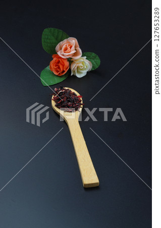 Karkade tea. Hibiscus tea leaves in wooden spoon isolated on wooden background. File contains clipping path. Top view. Selective focus. 127653289