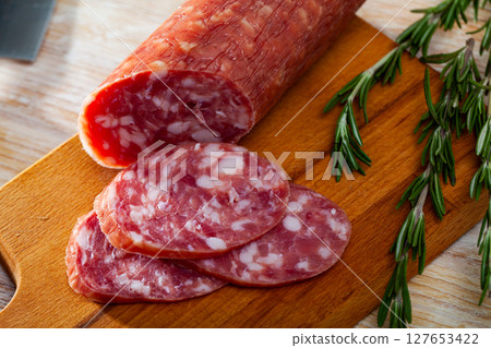 Thin salchichon sausage slices on wooden background, view from above 127653422