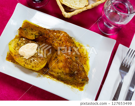 Baked chicken with sauce and potatoes at plate on table 127653499