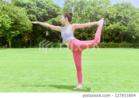 A woman doing yoga and pilates in a resort atmosphere under natural grass and blue skies A woman doing yoga and pilates in a resort atmosphere under natural grass and blue skies 127653804