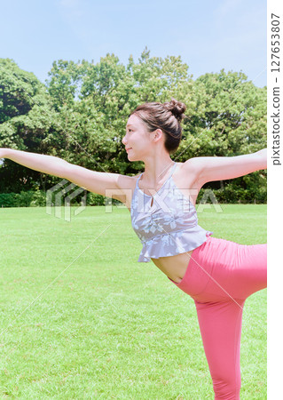 A woman doing yoga and pilates in a resort atmosphere under natural grass and blue skies 127653807
