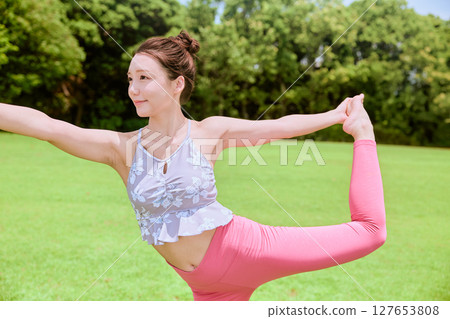 A woman doing yoga and pilates in a resort atmosphere under natural grass and blue skies A woman doing yoga and pilates in a resort atmosphere under natural grass and blue skies 127653808