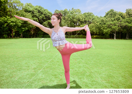 A woman doing yoga and pilates in a resort atmosphere under natural grass and blue skies 127653809