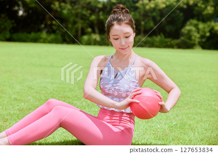 A woman doing yoga and pilates in a resort atmosphere under natural grass and blue skies 127653834