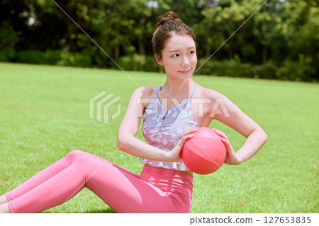 A woman doing yoga and pilates in a resort atmosphere under natural grass and blue skies 127653835