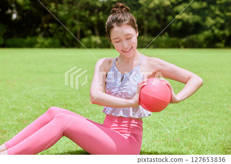 A woman doing yoga and pilates in a resort atmosphere under natural grass and blue skies 127653836