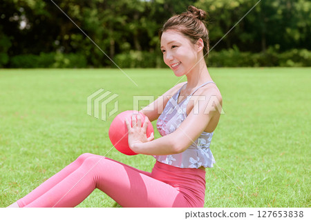 A woman doing yoga and pilates in a resort atmosphere under natural grass and blue skies A woman doing yoga and pilates in a resort atmosphere under natural grass and blue skies 127653838