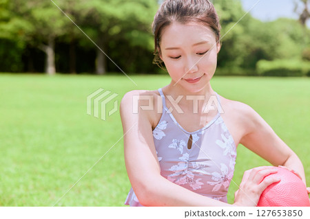 A woman doing yoga and pilates in a resort atmosphere under natural grass and blue skies A woman doing yoga and pilates in a resort atmosphere under natural grass and blue skies 127653850