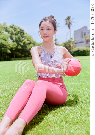 A woman doing yoga and pilates in a resort atmosphere under natural grass and blue skies 127653858