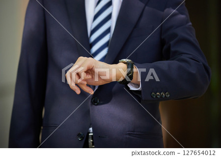 A young businessman in a suit looking at his watch in a business district A young businessman in a suit looking at his watch in a business district 127654012