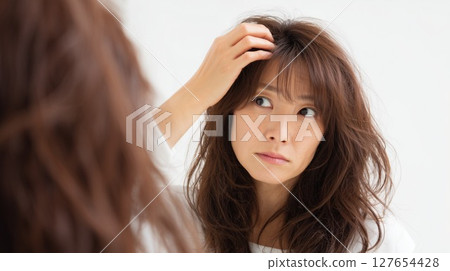 A woman in her 40s who is concerned about her hair quality 127654428