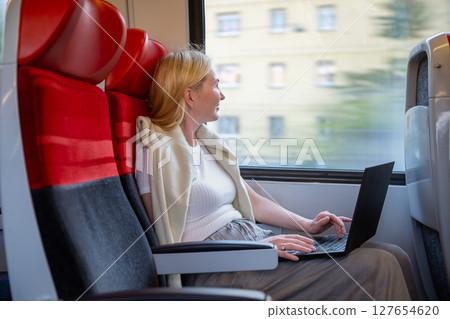 Woman working on laptop while traveling by train in daylight, concept of remote work and travel 127654620
