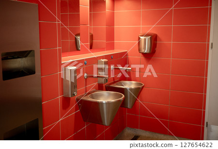 Modern public restroom with red tiled walls and stainless steel sinks 127654622